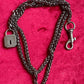 Vintage Saint Laurent upcycled necklace featuring a dark gunmetal chain with original lock and key charm pendant, repurposed from a Saint Laurent keychain, photographed on a red background