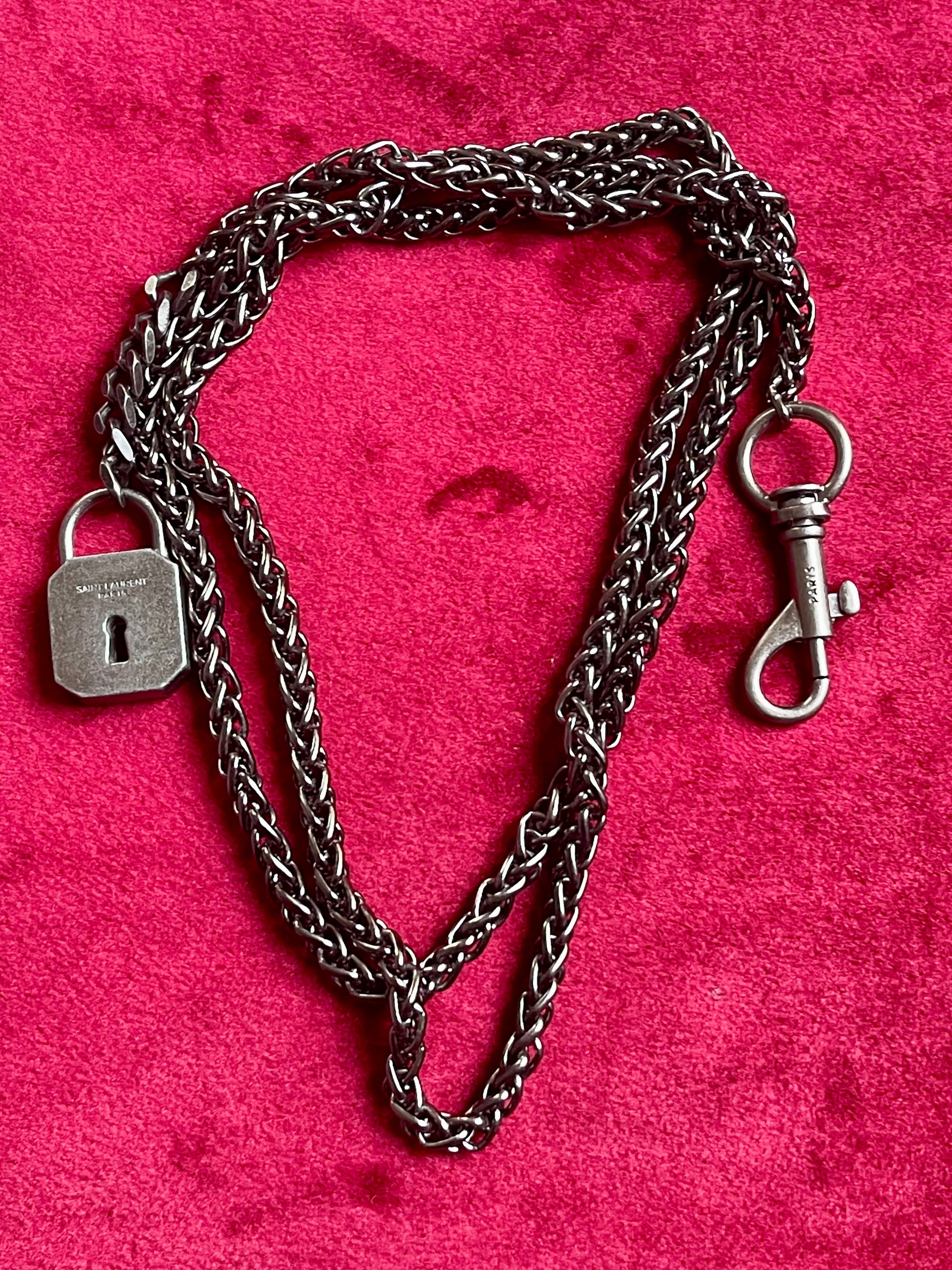 Vintage Saint Laurent upcycled necklace featuring a dark gunmetal chain with original lock and key charm pendant, repurposed from a Saint Laurent keychain, photographed on a red background