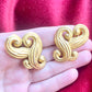 Close-up of vintage Nina Ricci swirly heart earrings in matte gold tone displayed on hand 