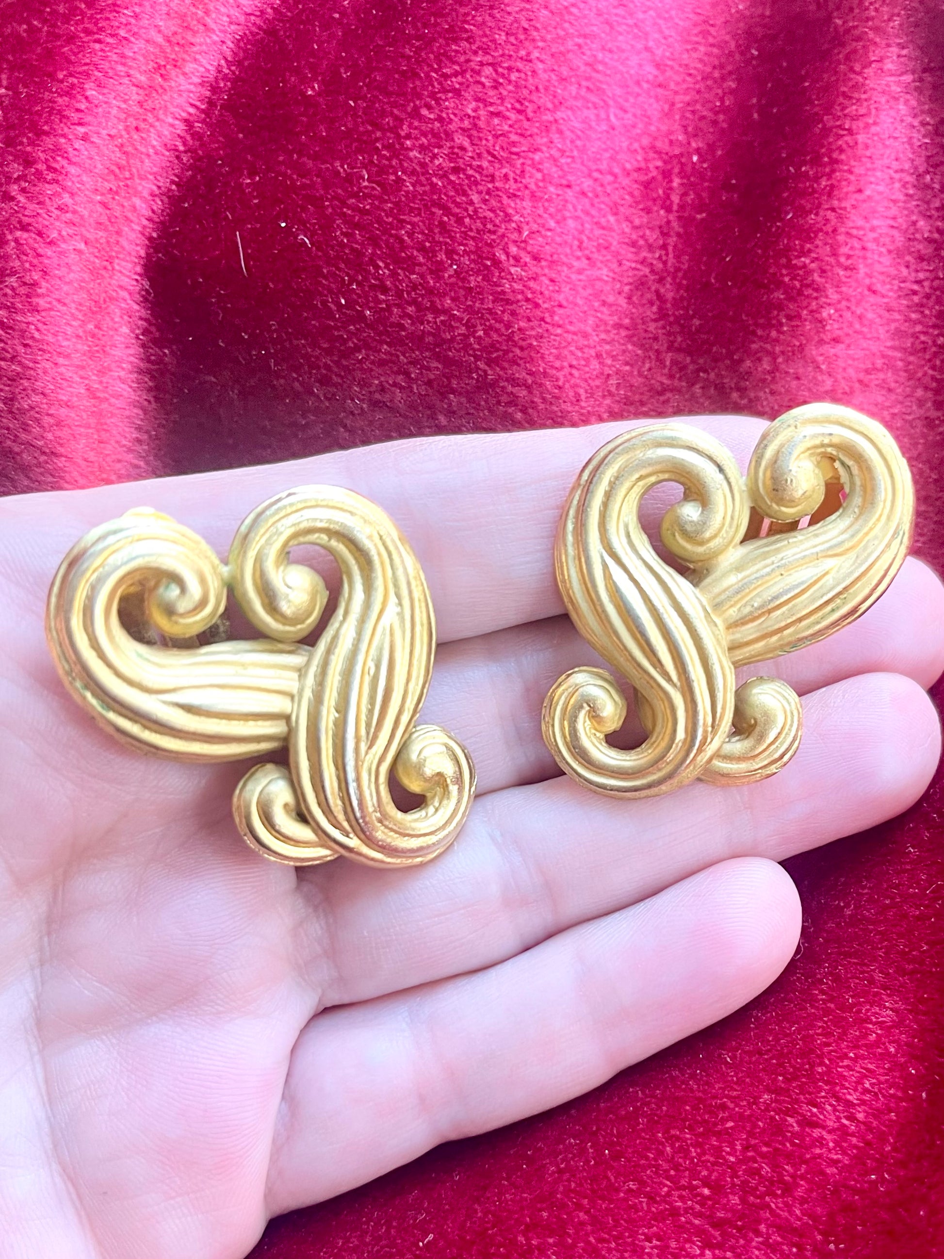 Close-up of vintage Nina Ricci swirly heart earrings in matte gold tone displayed on hand 