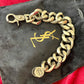 YSL chunky chain displayed draped on a sleek black Yves Saint Laurent pouch, showcasing bronze and grey tones