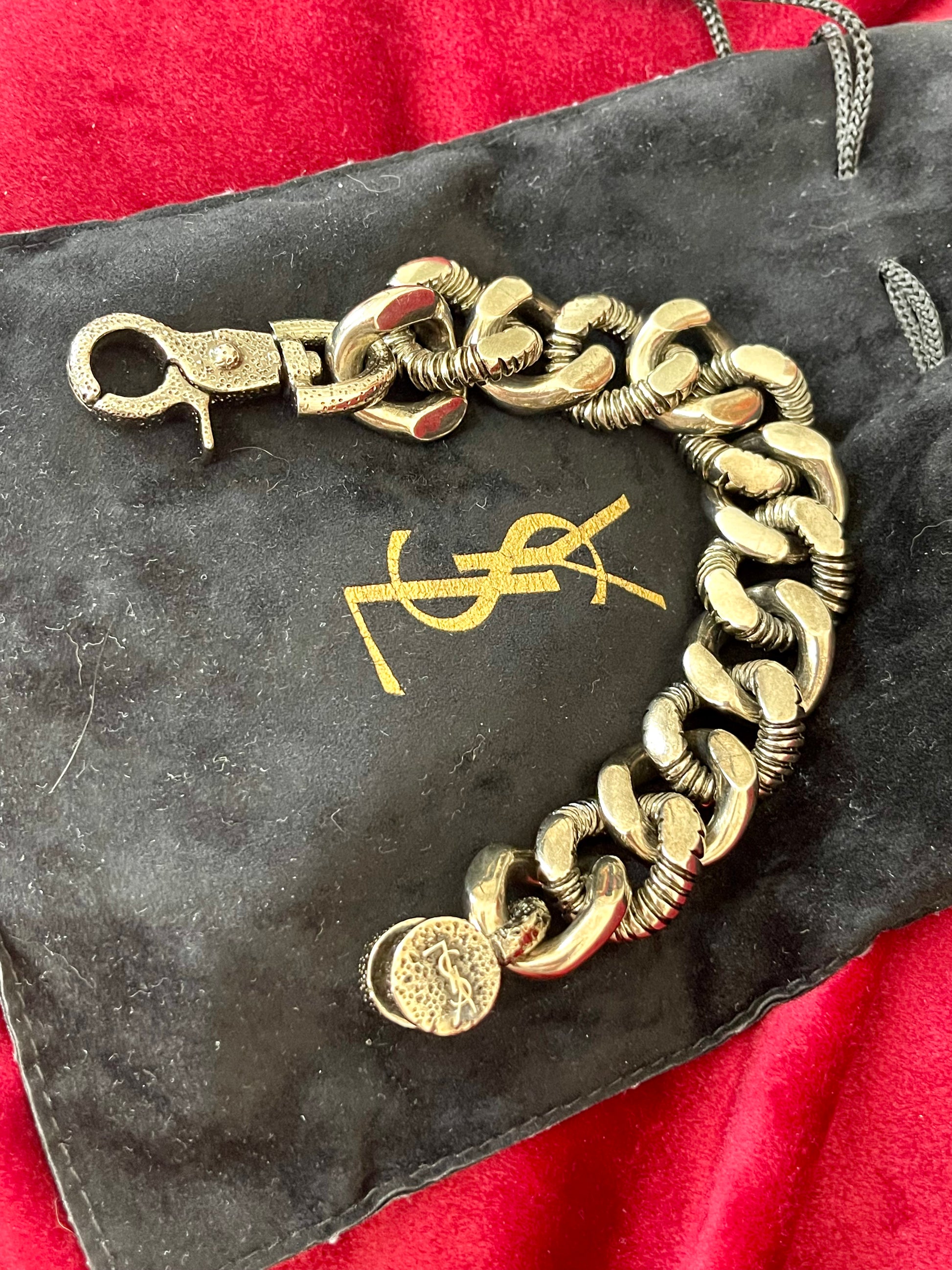 YSL chunky chain displayed draped on a sleek black Yves Saint Laurent pouch, showcasing bronze and grey tones