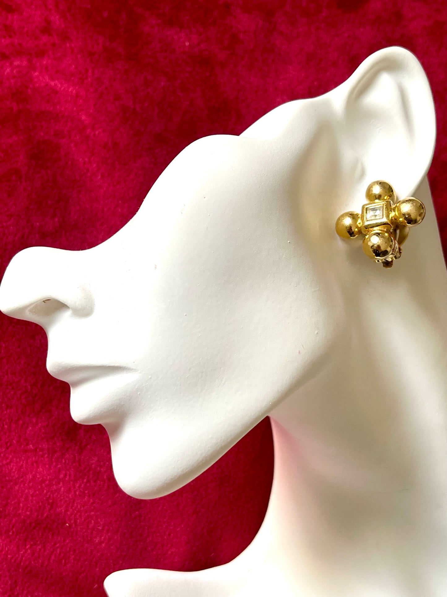 On white model Yves Saint Laurent vintage gold tone cross clip-on earrings from the 1980s, showing rounded gold domes and square-cut center stones