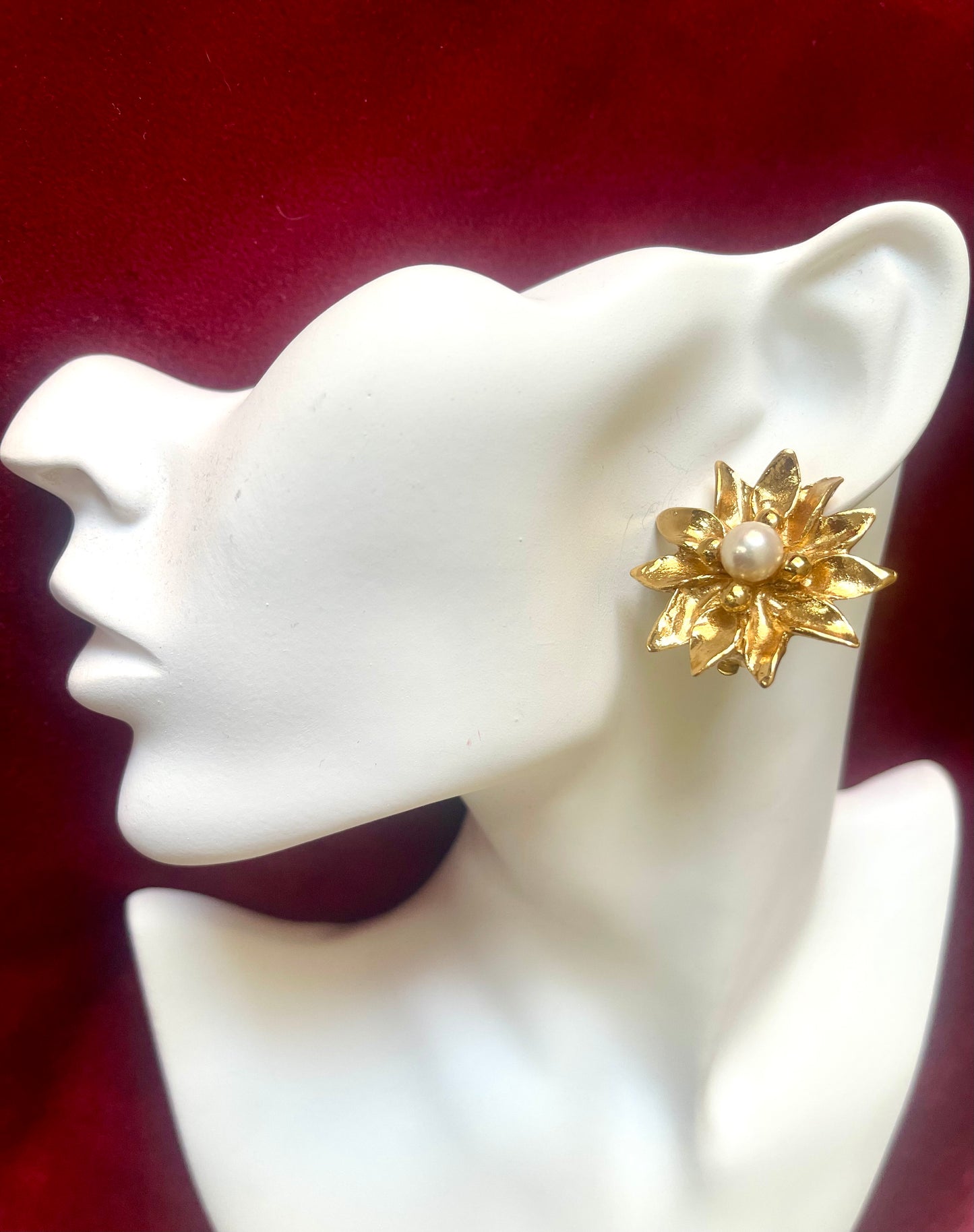 Yves Saint Laurent vintage 80s Gold flower-shaped earring with pearl center on a white mannequin ear against a red background