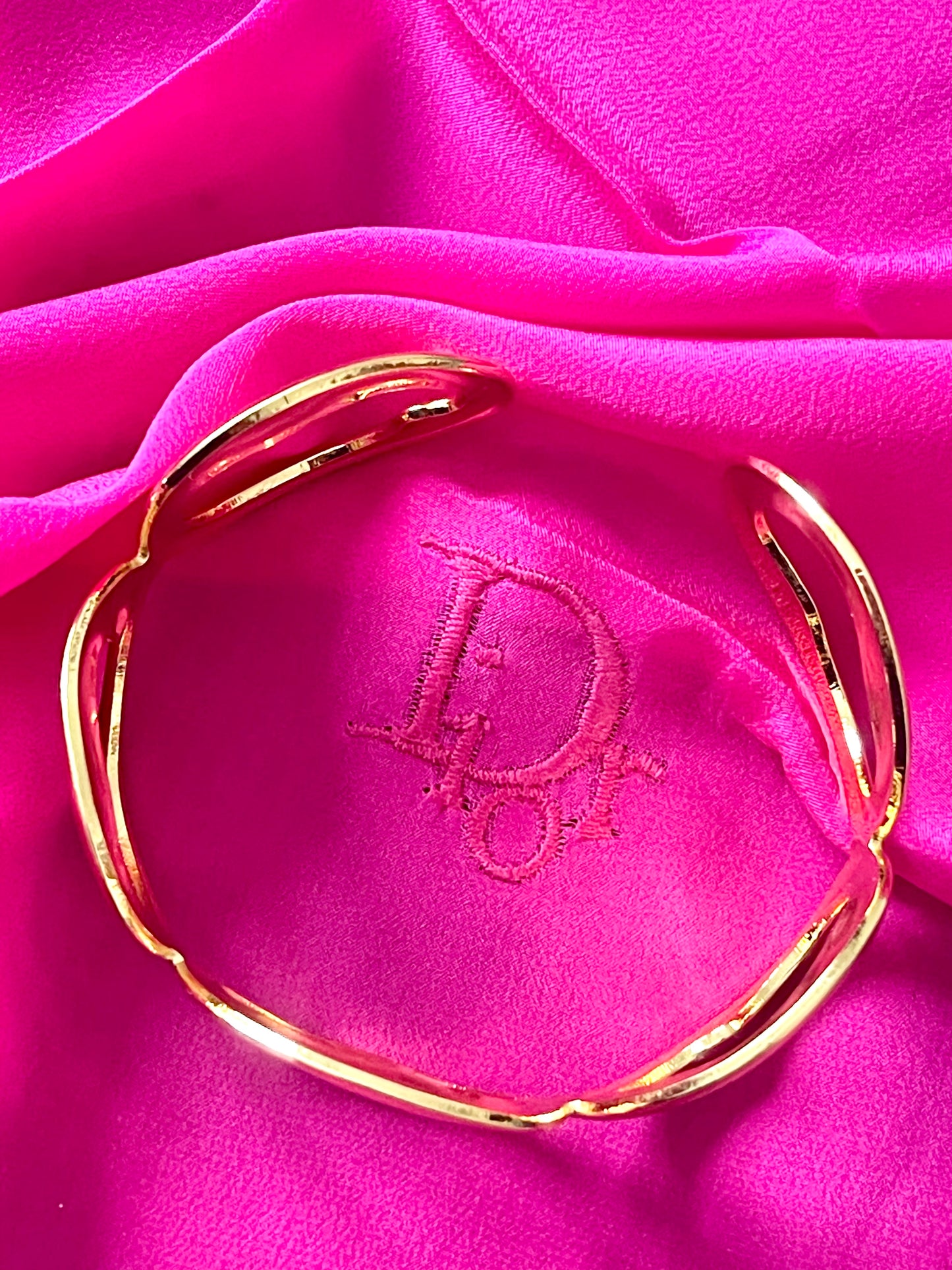 Gold bracelet on a pink fabric background with Christian Dior logo