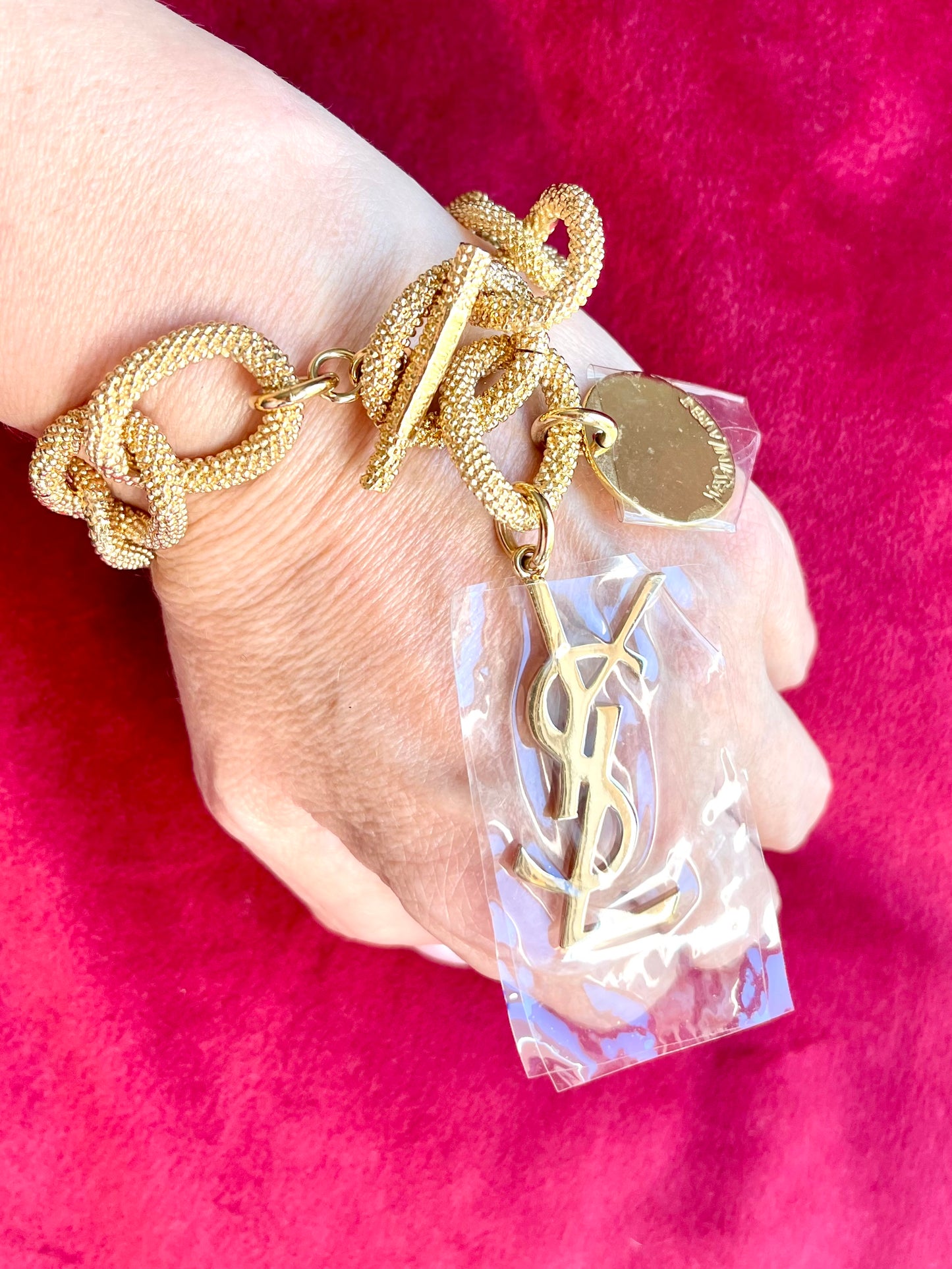 Gold-tone vintage YSL chain bracelet worn on wrist with YSL logo charm and medallion