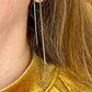 Gold chain earring with a YSL logo worn by a person with long hair, wearing a mustard yellow top.