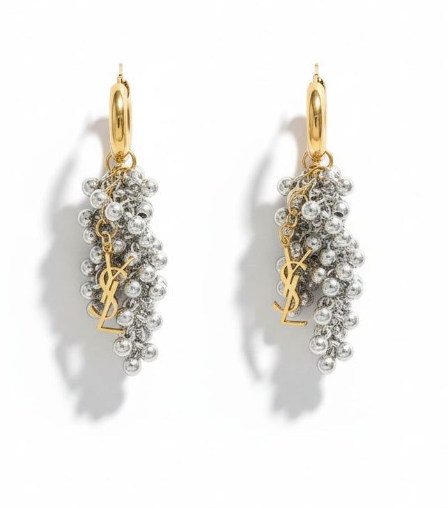 Gold and silver earrings with pearl-like beads and YSL Yves Saint Laurent charms on a white background