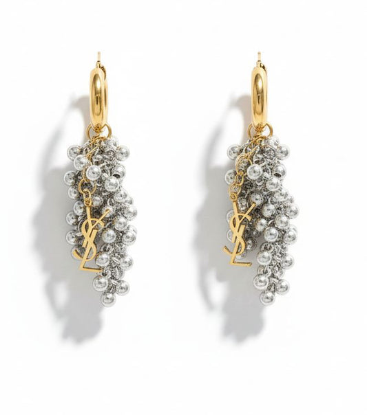 Gold and silver earrings with pearl-like beads and YSL Yves Saint Laurent charms on a white background